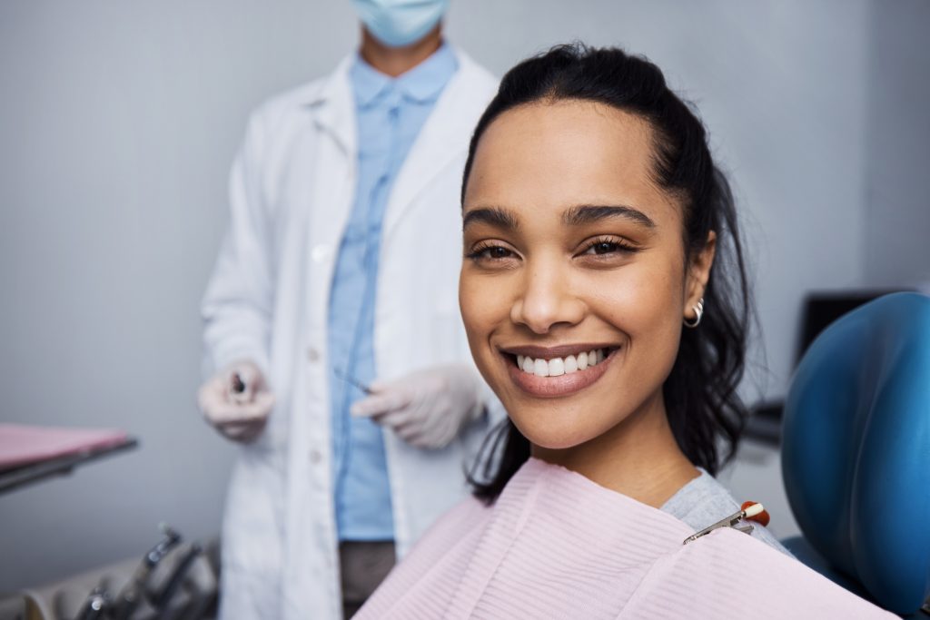 Mujer sonriendo sentada en silla de dentista, dentro de un consultorio con odontólogo detrás