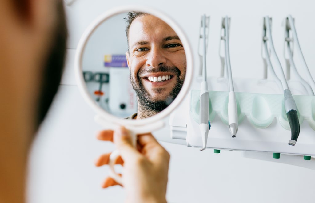 Hombre mirando en el espejo su sonrisa con limpieza dental