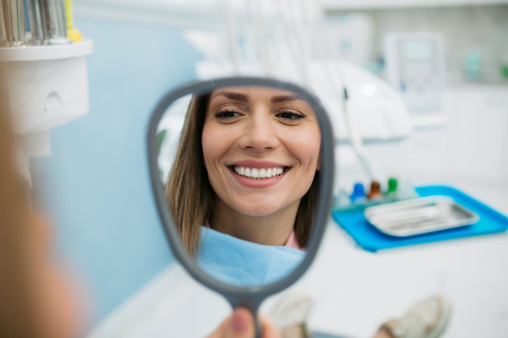 Mujer apreciando su sonrisa en el espejo, después de un blanqueamiento dental